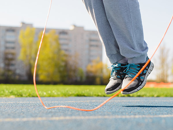 Close-up of lower body jumping rope, exercising on sports ground outdoors on sunny day.